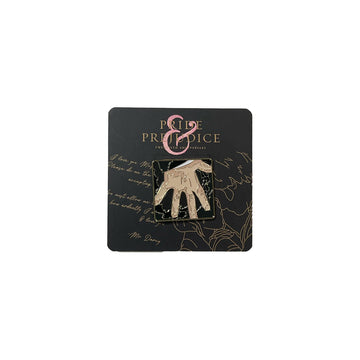 A gold-colored enamel pin in the shape of Mr. Darcy's hand from the Pride & Prejudice film, mounted on a black backing with the film's title. Celebrate the 20th anniversary of the Oscar-nominated film Pride & Prejudice (2005). Together with Focus Features the Academy Museum Store